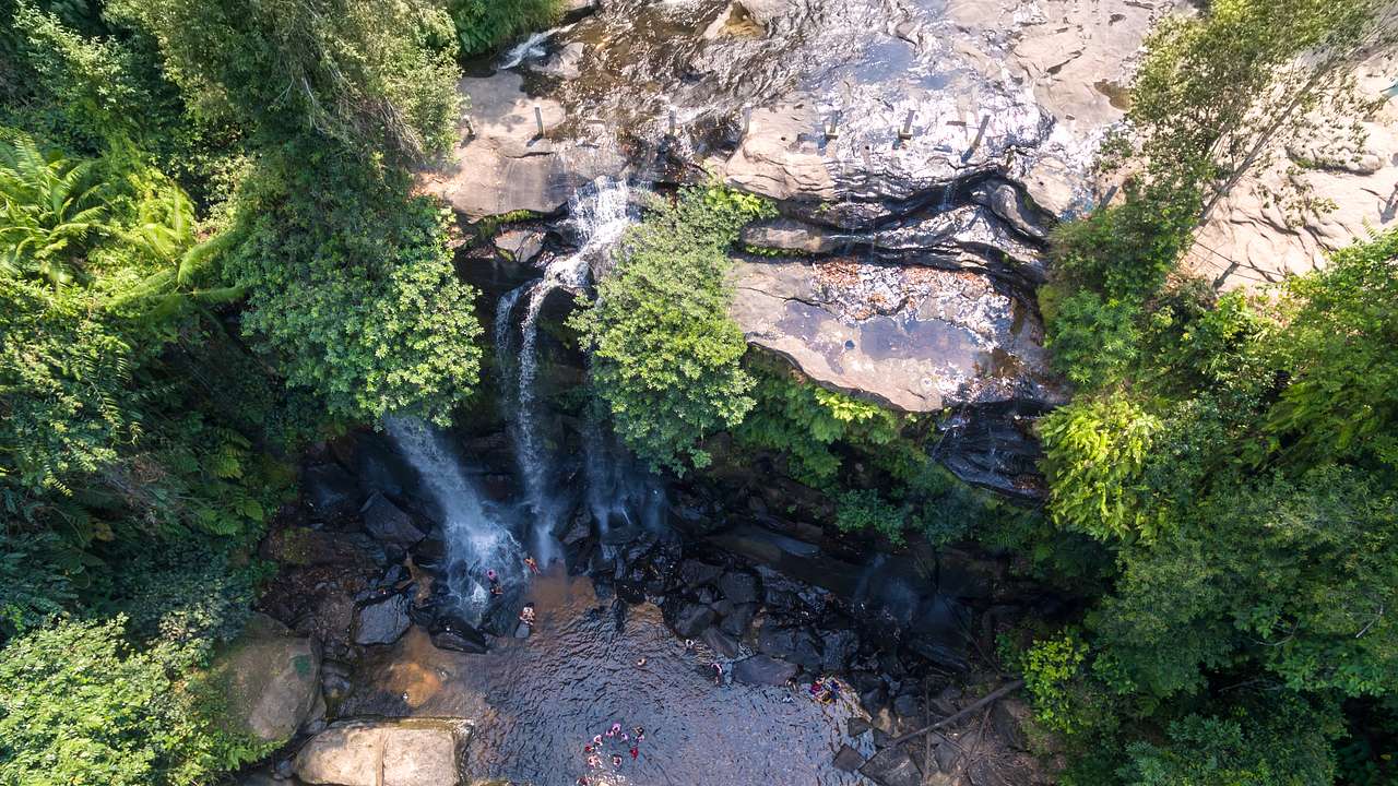 An aerial shot of a small waterfall cascading over a cliff amongst trees