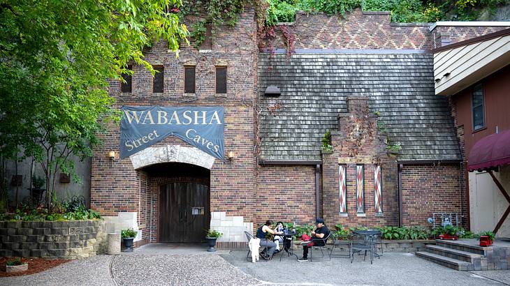 An entrance of a brick wall facade with a "Wabasha Street Caves" sign next to a tree