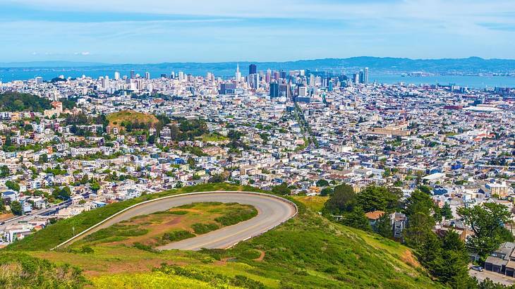 A green hilltop with a curved path and a view of a city on a clear day A green hilltop with a curved path and a view of a city on a clear day