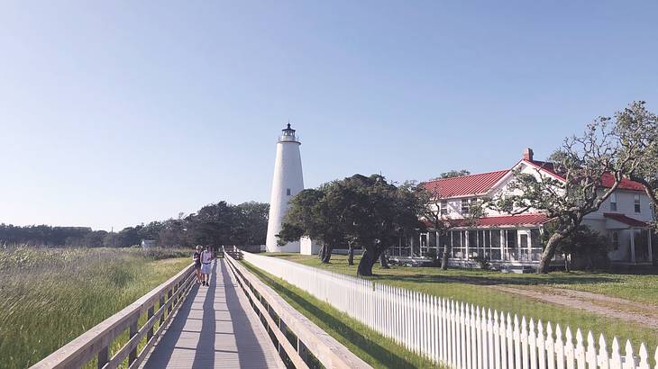 A boardwalk leading to a white lighthouse with a building on the right