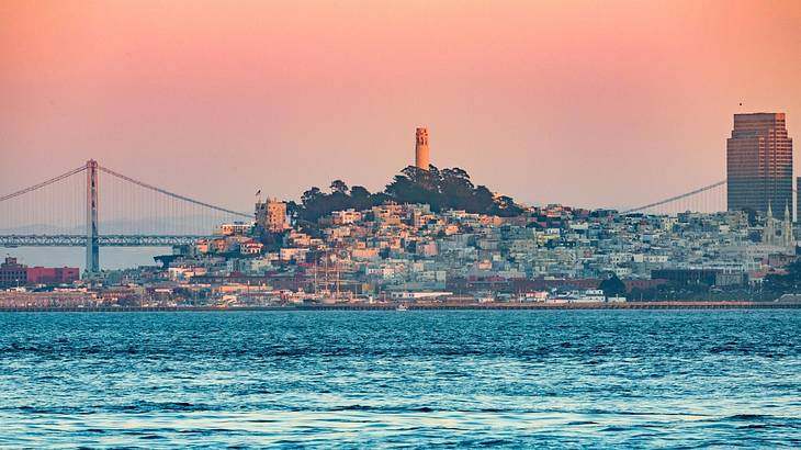 A view of a bridge and an island with ocean water in front of it at sunset A view of a bridge and an island with ocean water in front of it at sunset