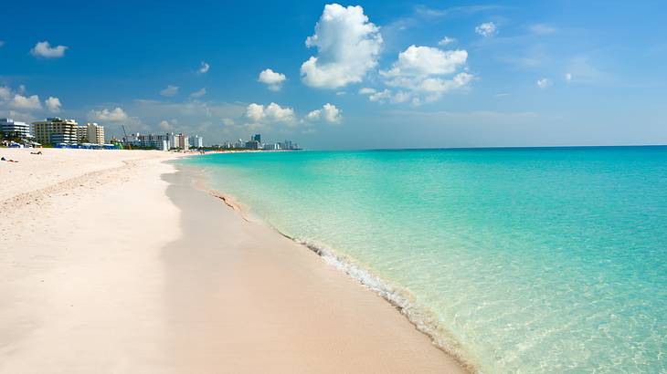 A white sand beach with crystal blue water and buildings in the distance