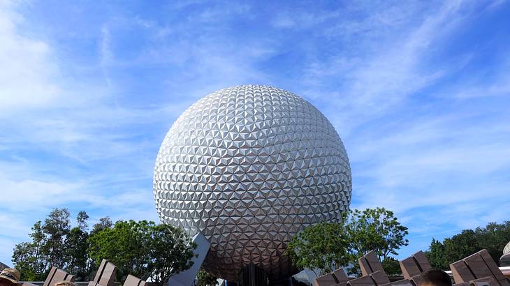 A large white metallic sphere propped by pillars above trees and other structures