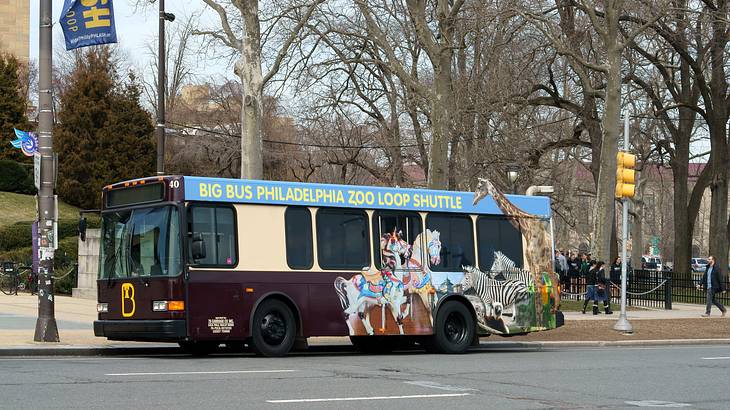 A maroon bus with animals and a "Philadelphia Zoo" sign