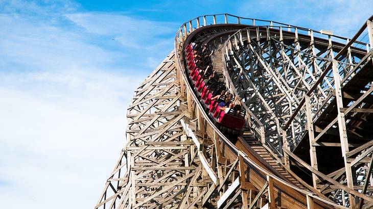 People riding a red roller coaster car on a wooden track from below People riding a red roller coaster car on a wooden track from below