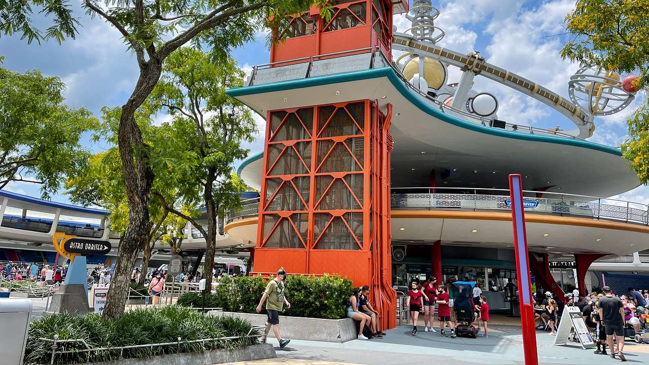 A red elevator tower surrounded by other structures, green trees, and people around