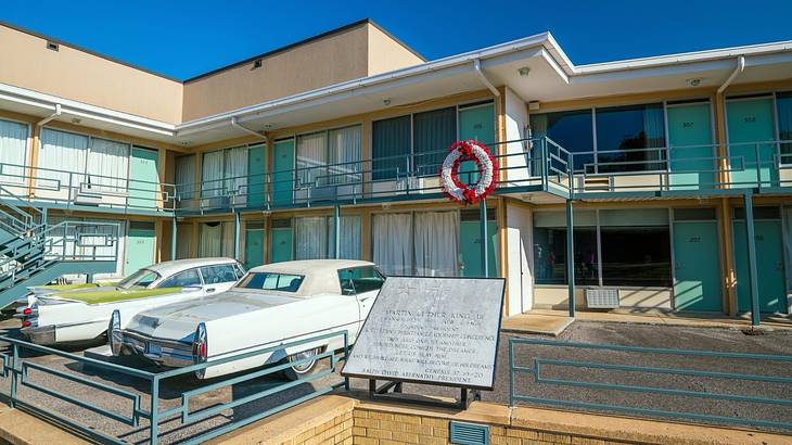 An old-fashioned motel with 1960s-style cars and a historical plaque in front of it