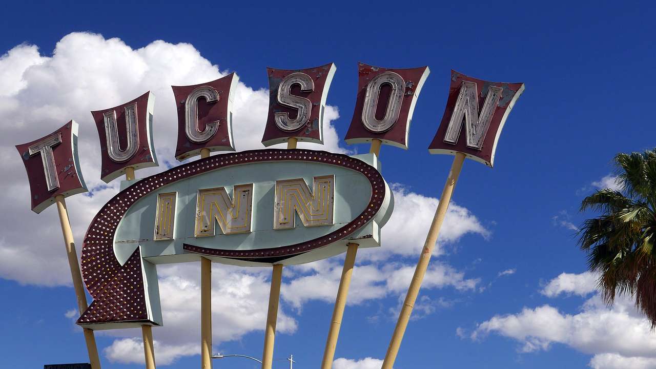 A sign which reads Tucson Inn next to a blue sky with white clouds