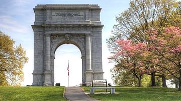 A stone arch with a flag in the middle next to the grass and trees
