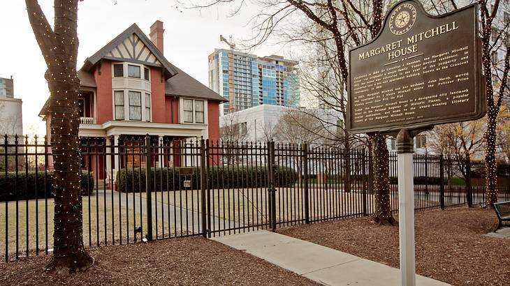 A gated house next to a sign that says "Margaret Mitchell House" with text below it