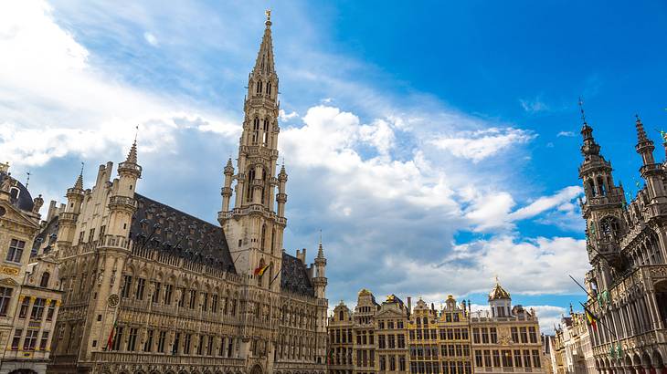 A large Gothic-style building next to a square under a blue sky with clouds