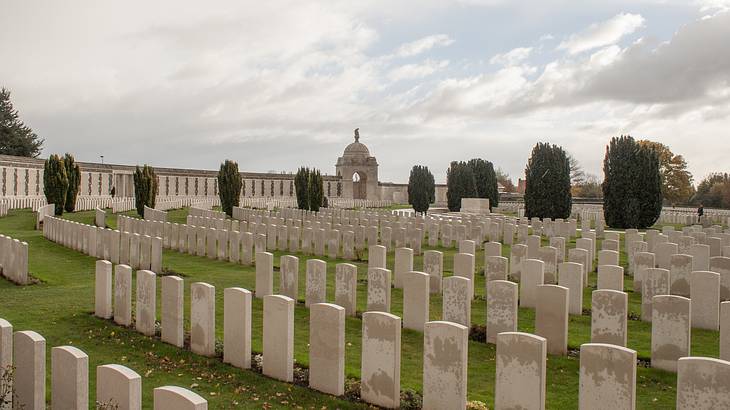 White tombstones lined up in rows on a grassy open area on a cloudy day