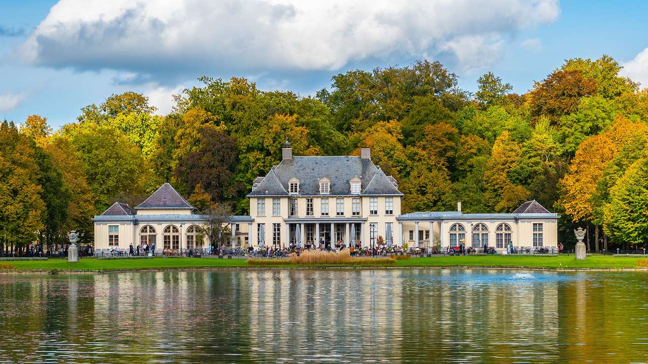 A mansion building surrounded by trees and a pond in front