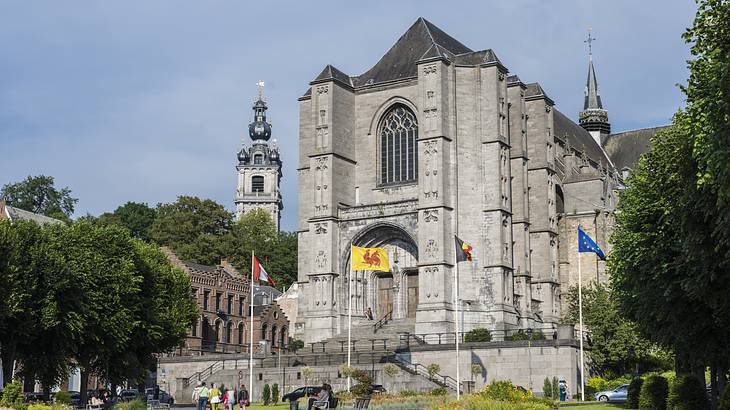 A stone church building with two towers next to grass and flags on an overcast day