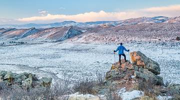 A hiker standing on a boulder surrounded by snow and mountains