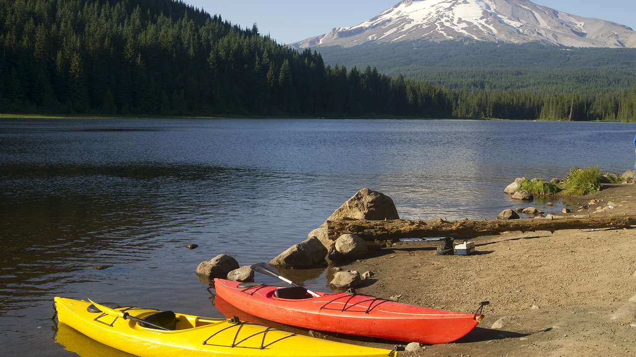 Two kayaks on the shore of a lake with a forest and snow-covered mountain behind