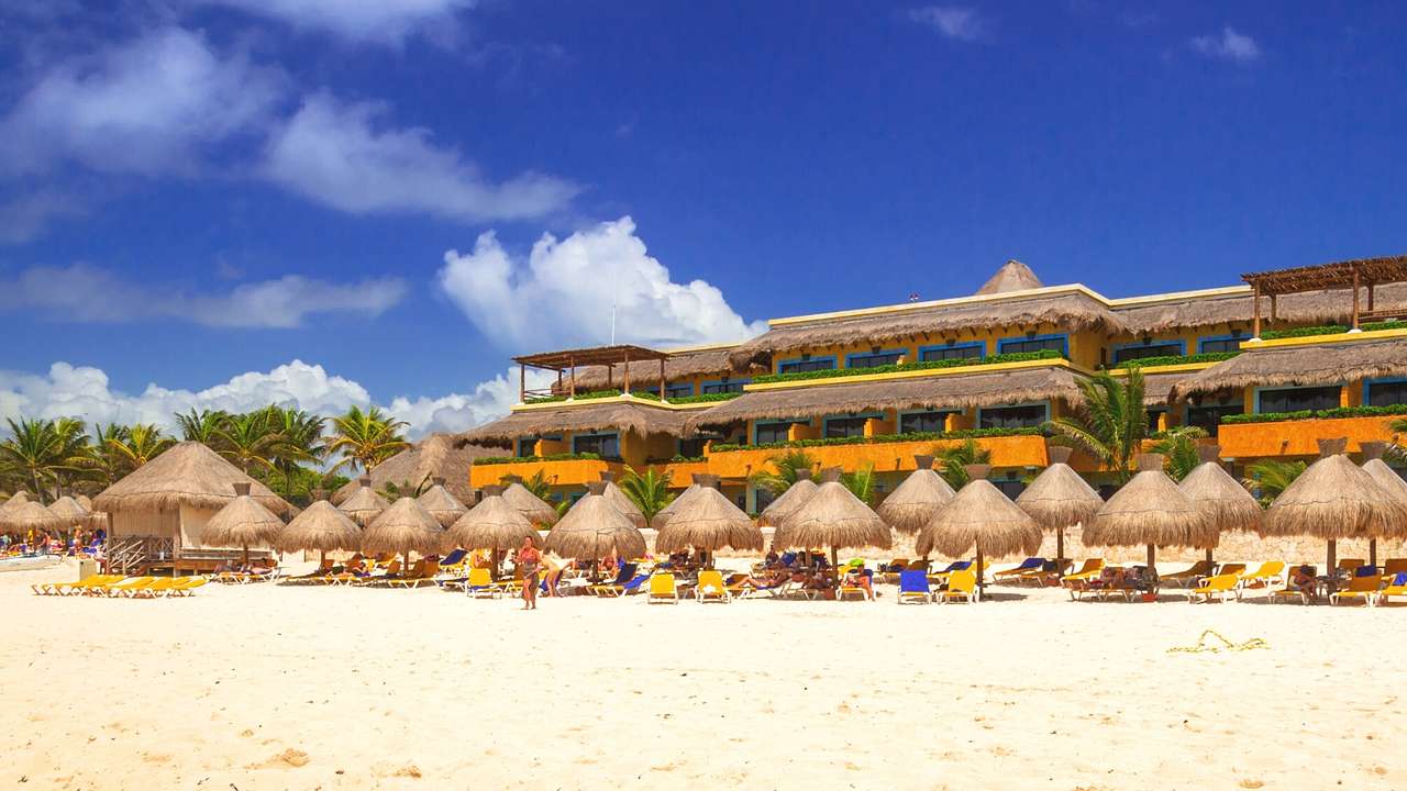 A sandy beach with tropical beach umbrellas next to a resort building