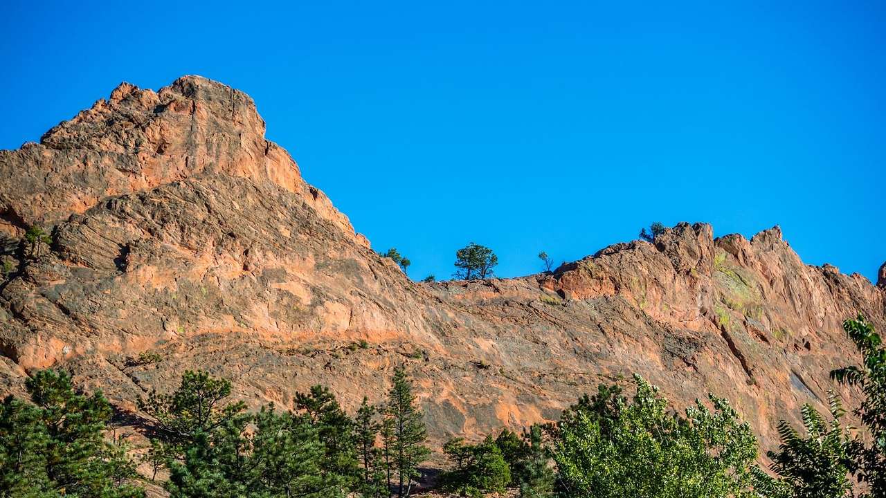 Red rock mountains with greenery below them and a blue sky above