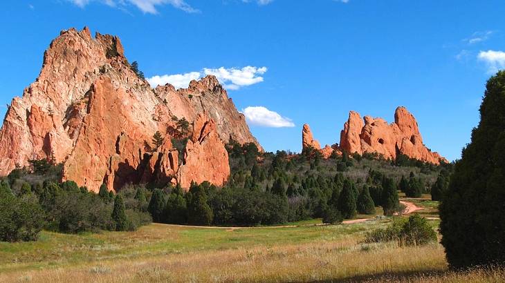 Red stone cliffs with green grass and trees in the foreground under blue sky