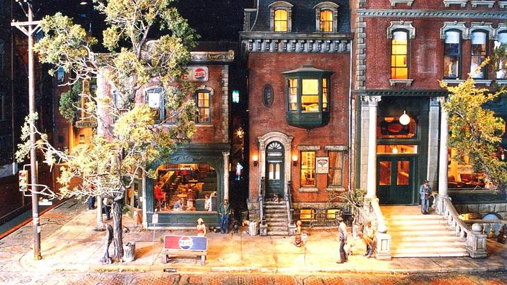 Figurines in a model village with brownstone houses and trees on the street