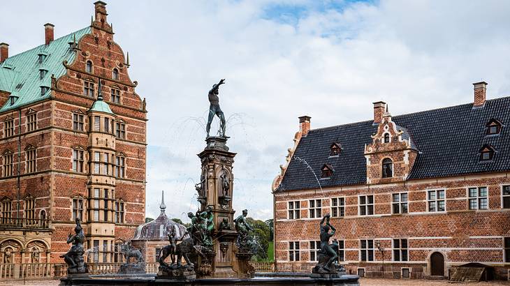 A large circular fountain with a man on top next to a tall brick building