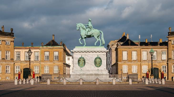 A statue of a man riding a horse on a podium with buildings in the background