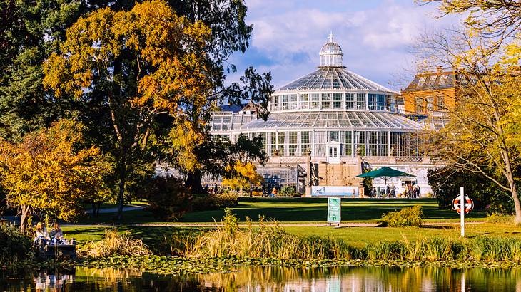 A dome glasshouse surrounded by trees and a lake in front