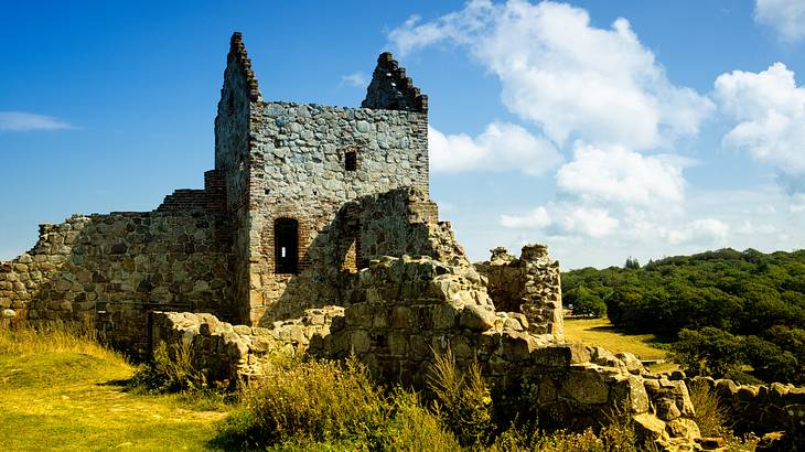 The ruins of a medieval stone castle next to grass and bushes