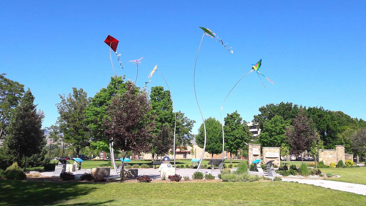 A sculpture with colorful kites surrounded by grass and trees under a blue sky