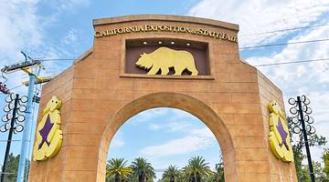A large archway with a bear symbol and a sign on it, with trees and exhibits behind