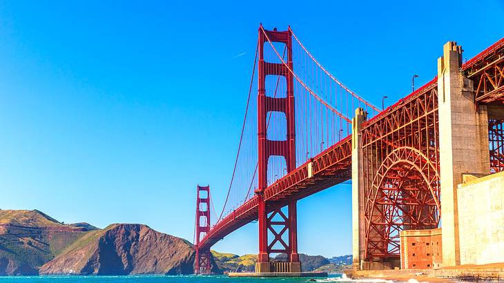A large red suspension bridge over the water with small hills on one side A large red suspension bridge over the water with small hills on one side