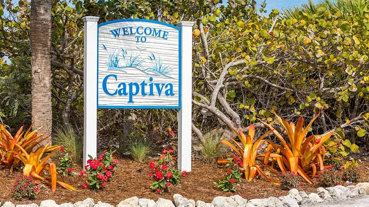 A "Welcome to Captiva" signboard with flowers on the ground, in front of green trees