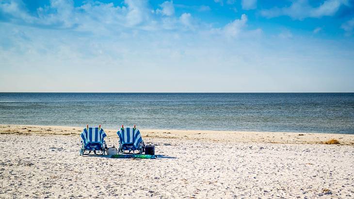 Looking towards a white sand beach with two beach chaise lounges against a sea