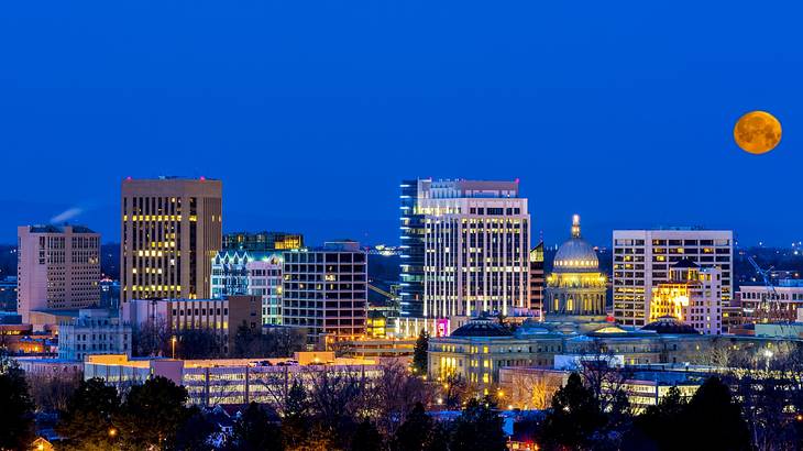 A view of a city illuminated at night under a dark blue sky with an orange moon