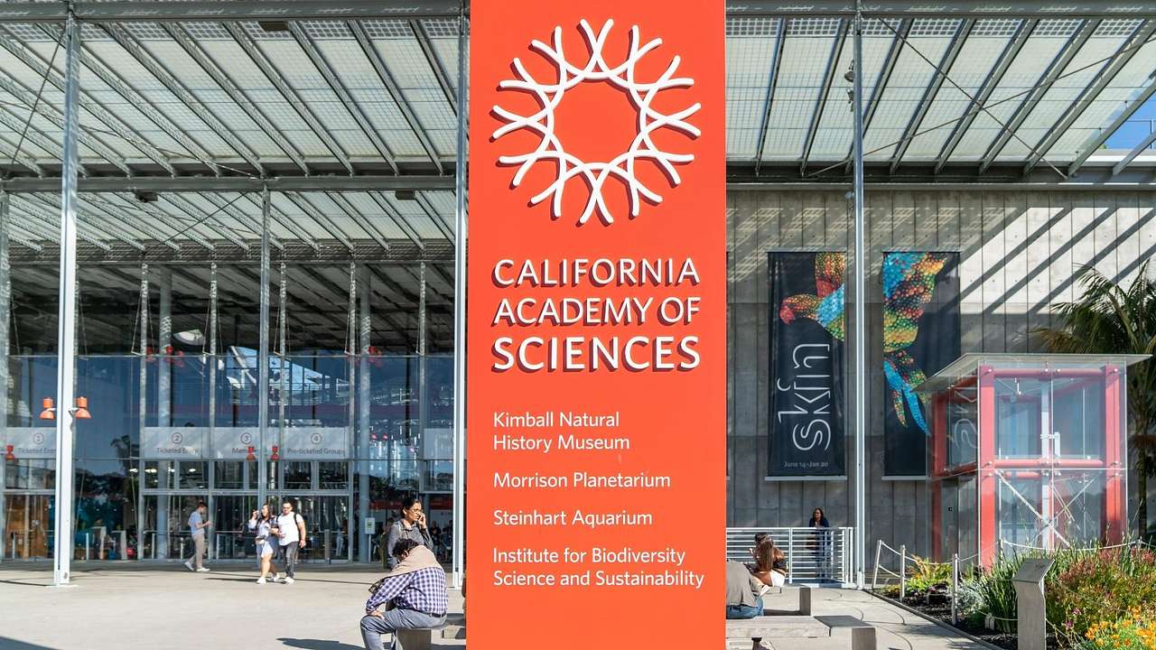 An orange "California Academy of Sciences" sign in front of a glass building