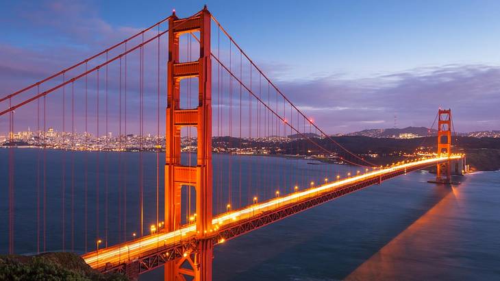 A red suspension bridge crossing a bay of water at night under a purple sky