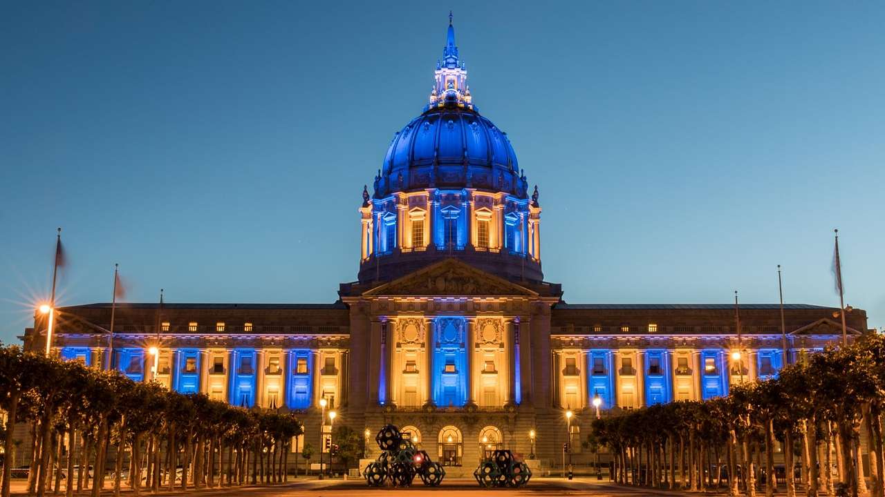 A large stone building with a domed roof lit up in yellow and blue at night