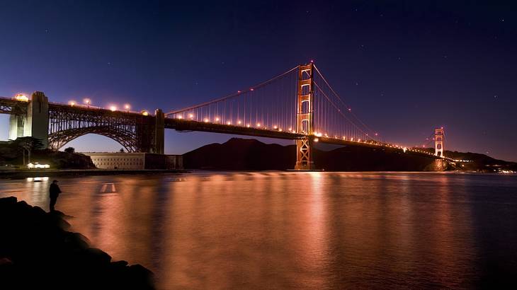 An illuminated suspension bridge over a body of water at night