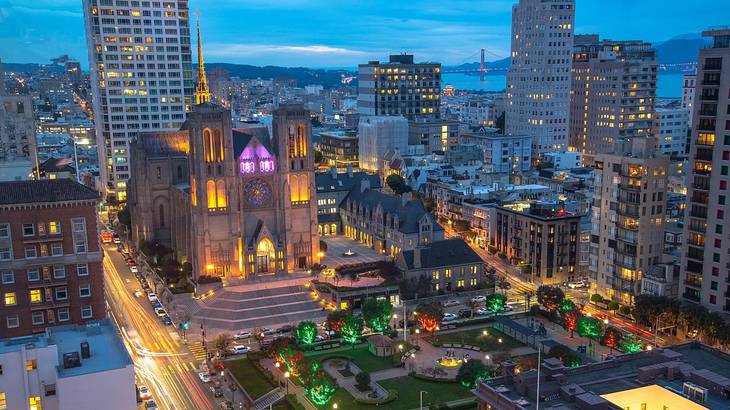 A cathedral with buildings around it and a park in front of it at night