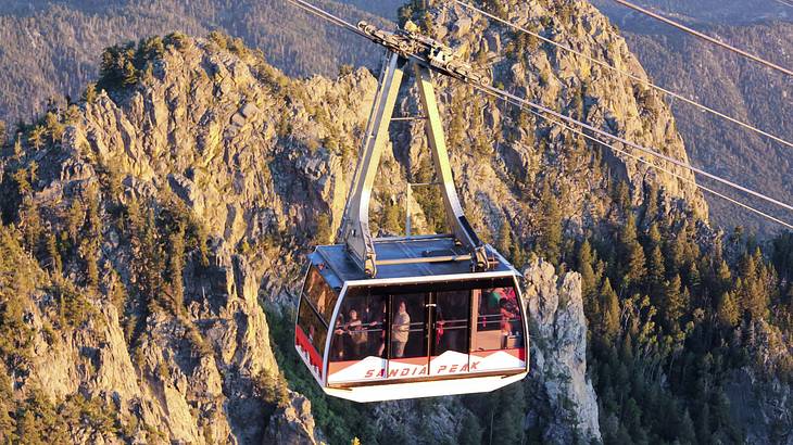 A cable car against tall and rugged mountains covered with green trees