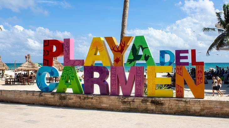 A colourful sign that spells "Playa del Carmen" next to a beach