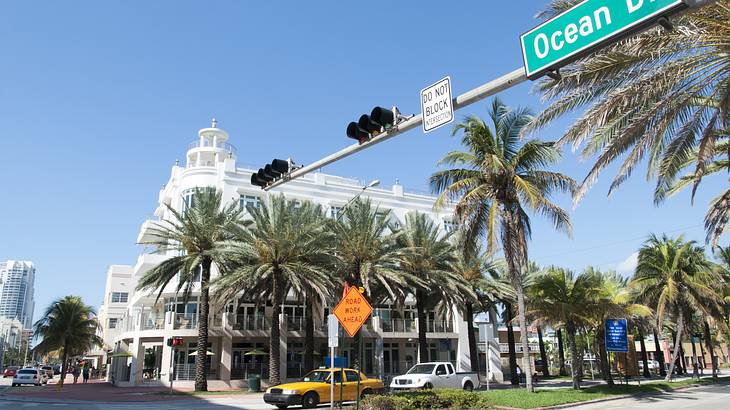 Traffic light with signage at an intersection, across buildings and palm trees
