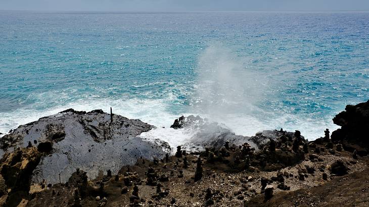 Black rocks with water spurting out of them and ocean behind
