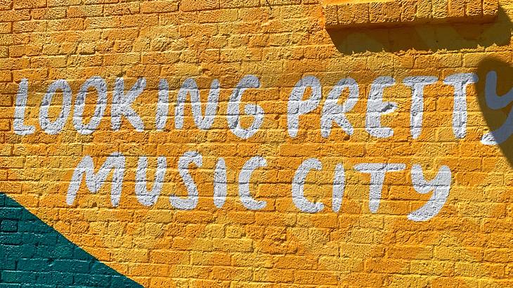 A brick wall painted yellow and a sign that says "Looking Pretty, Music City"