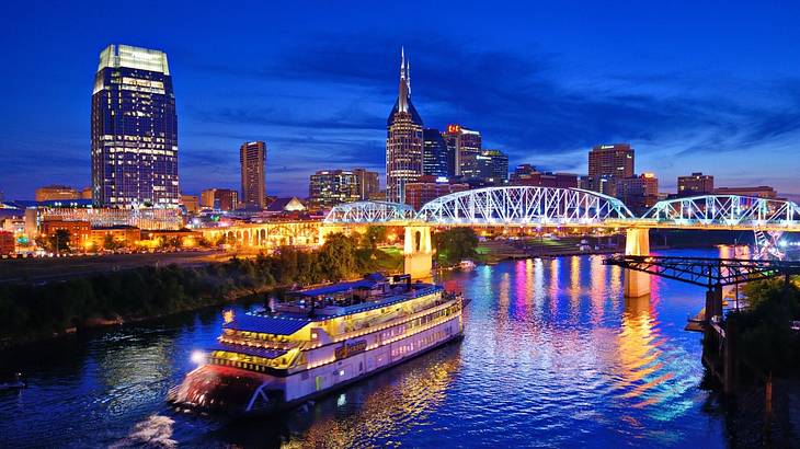 A cruise boat on a river with illuminated buildings surrounding it at night