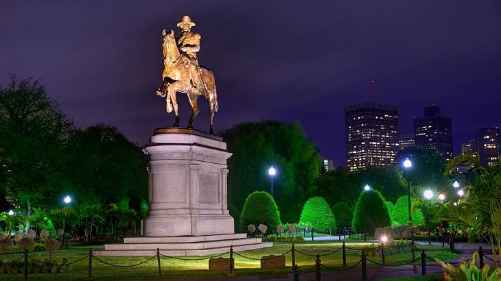 A statue of a man on a horse in an urban park at night