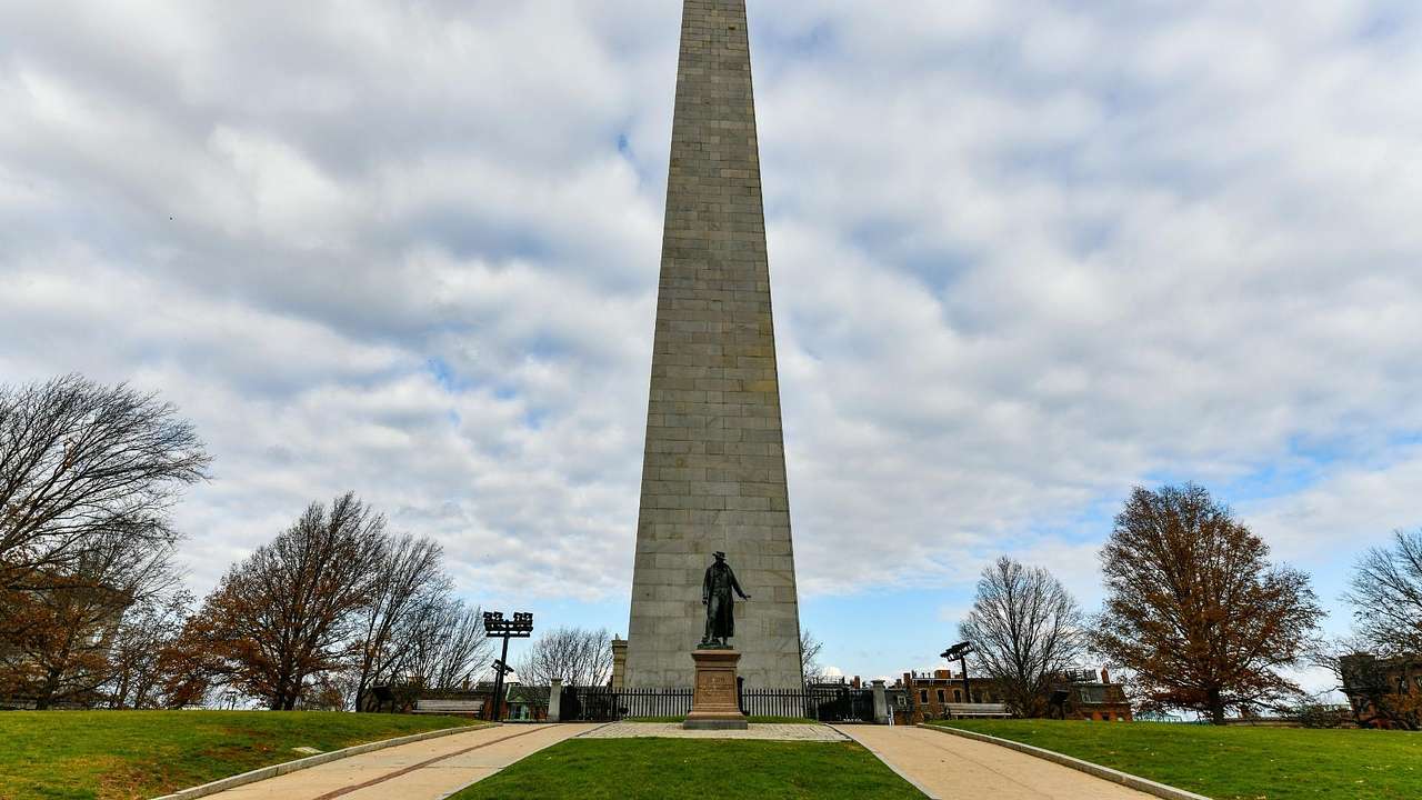 An obelisk monument with a statue of a man on the grass in front of it