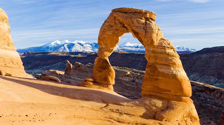 An orange rock arch formation with mountains in the background