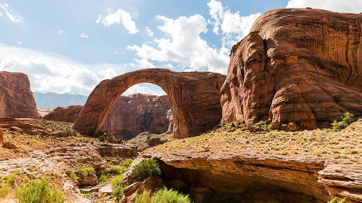 A red rock arch with cliffs surrounding it under a blue sky with clouds