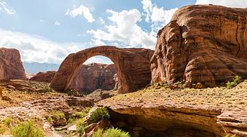 A red rock arch with cliffs surrounding it under a blue sky with clouds